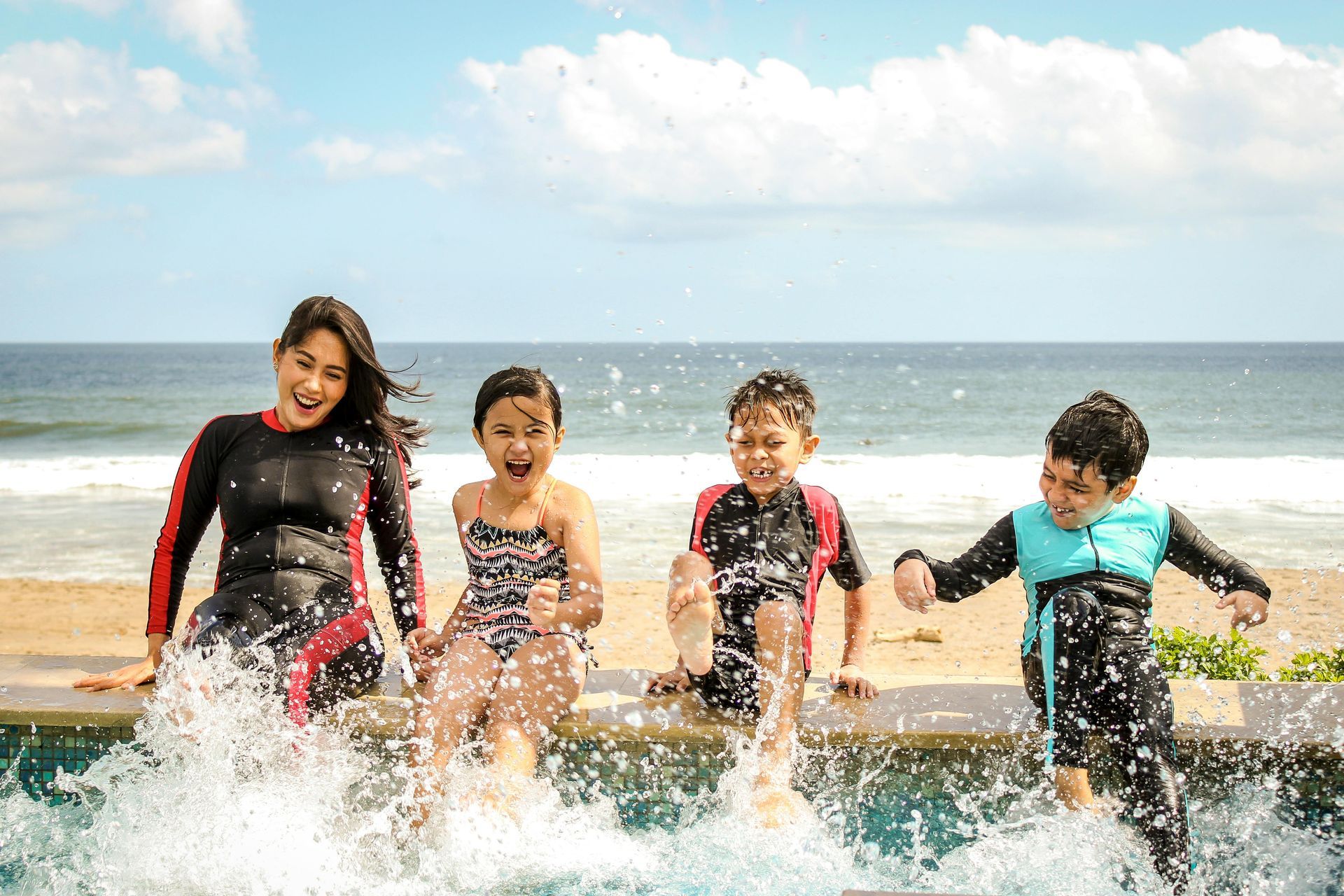 Woman and three children splashing in water near the ocean.
